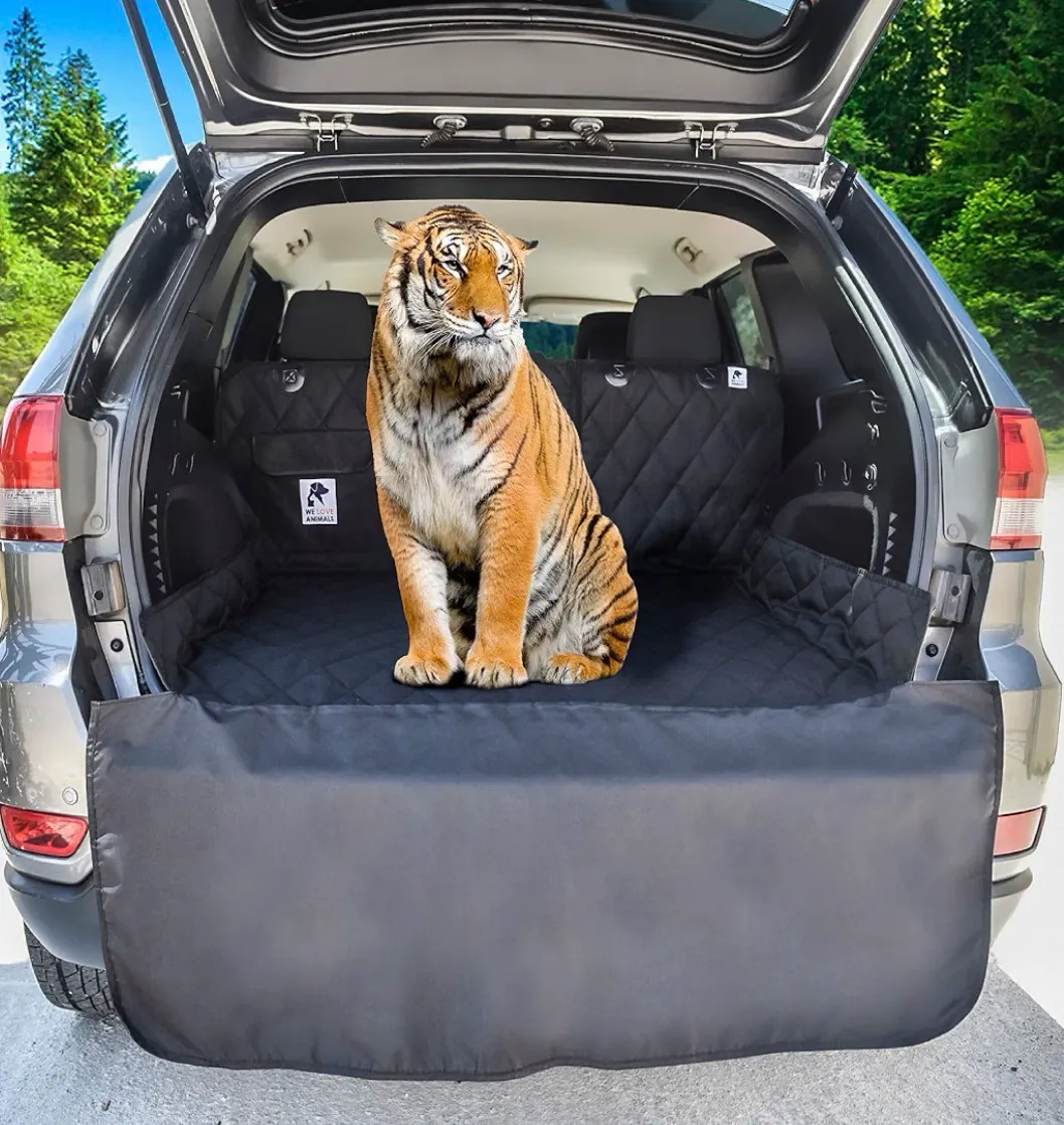 A product listing photo of a black quilted cargo liner installed in an SUV trunk, with a full-grown tiger sitting calmly on top of it.